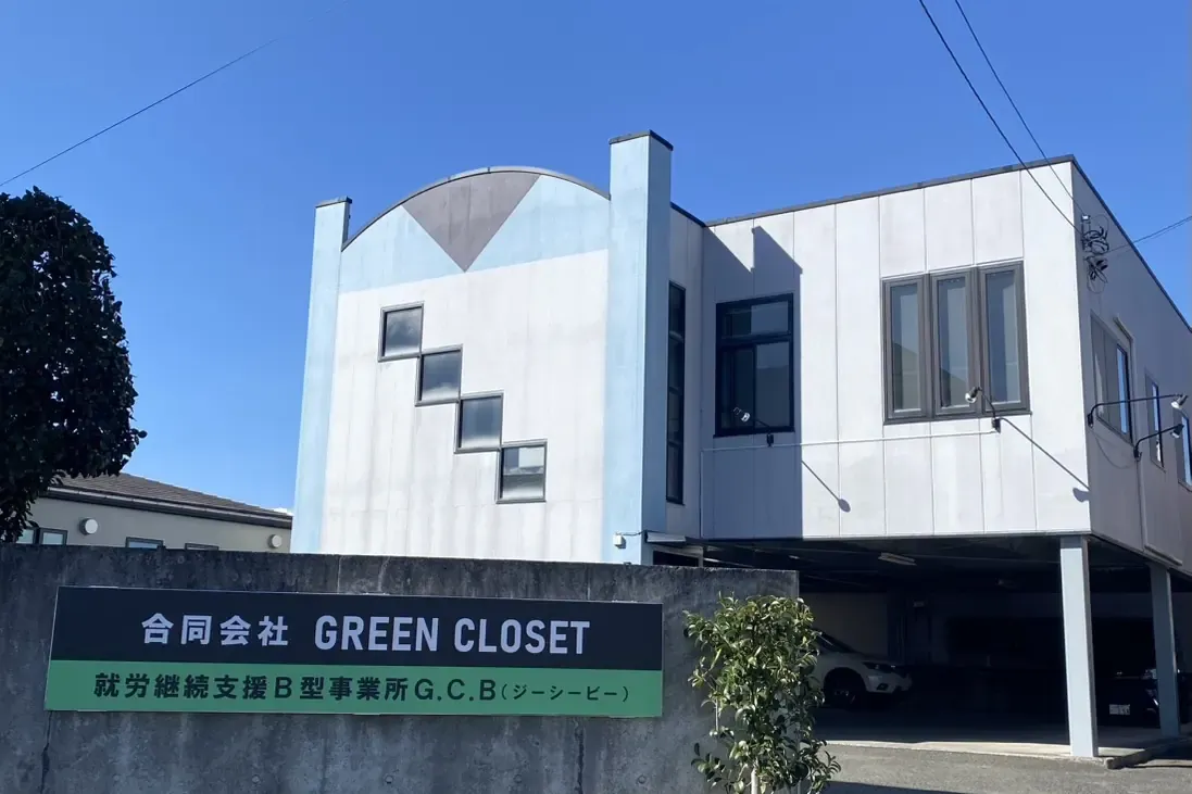 合同会社GREEN CLOSETの事業所外観。「合同会社 GREEN CLOSET／就労継続支援B型事業所 G.C.B（ジーシービー）」と記された看板が建物の前に立っている