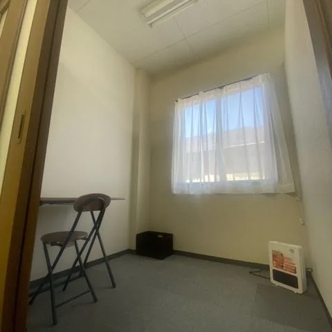 窓のある個室の室内。デスクと椅子が置かれている